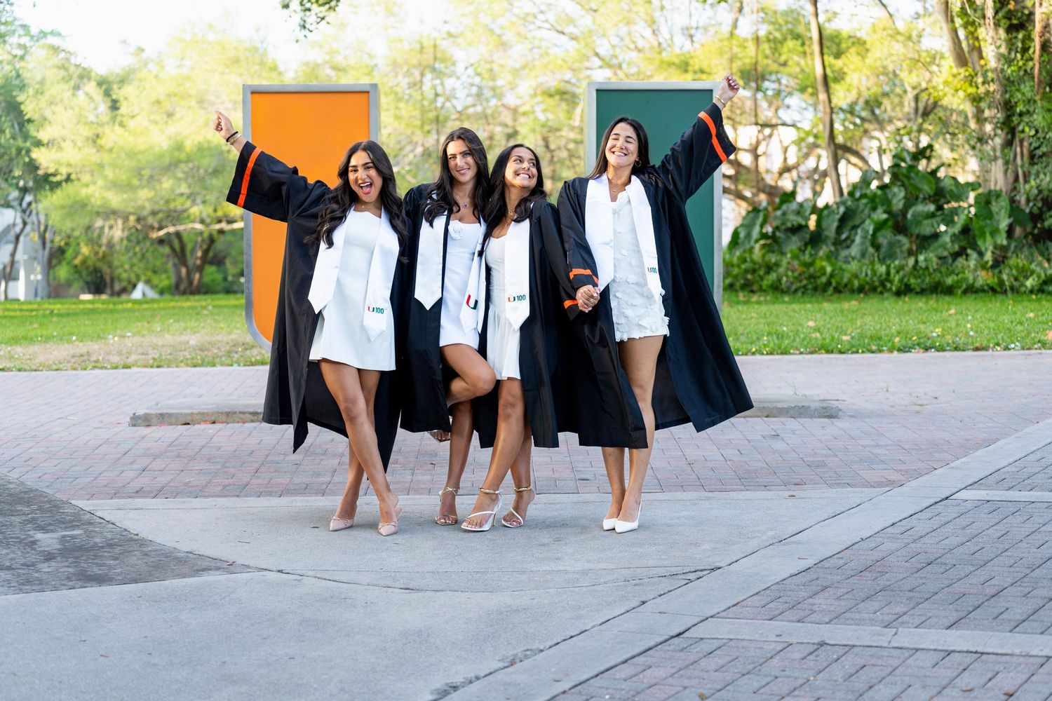 Graduates in black robes and caps celebrate their commencement while walking along a paved outdoor path.