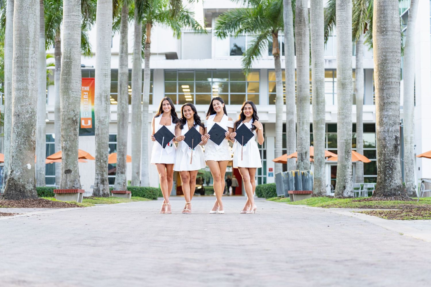 Five people in matching dresses walk through a palm tree lined path on a bright sunny day.