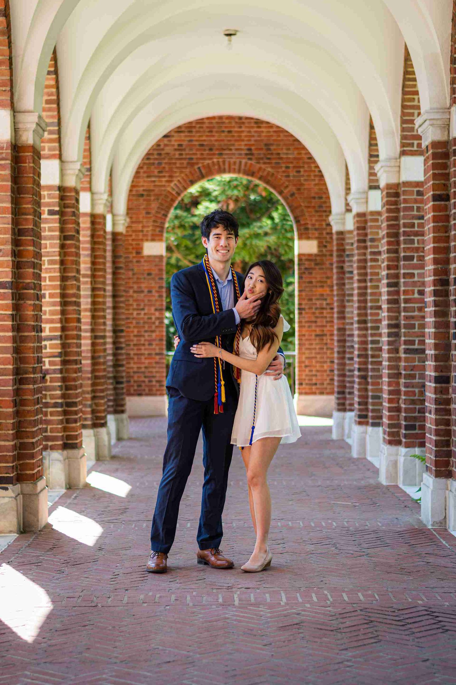 Couple poses together under a classic brick colonnade with arched ceilings.