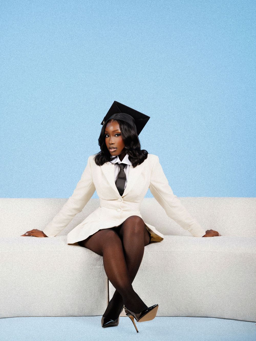 A person in a white blazer poses gracefully against a minimalist white and blue backdrop.