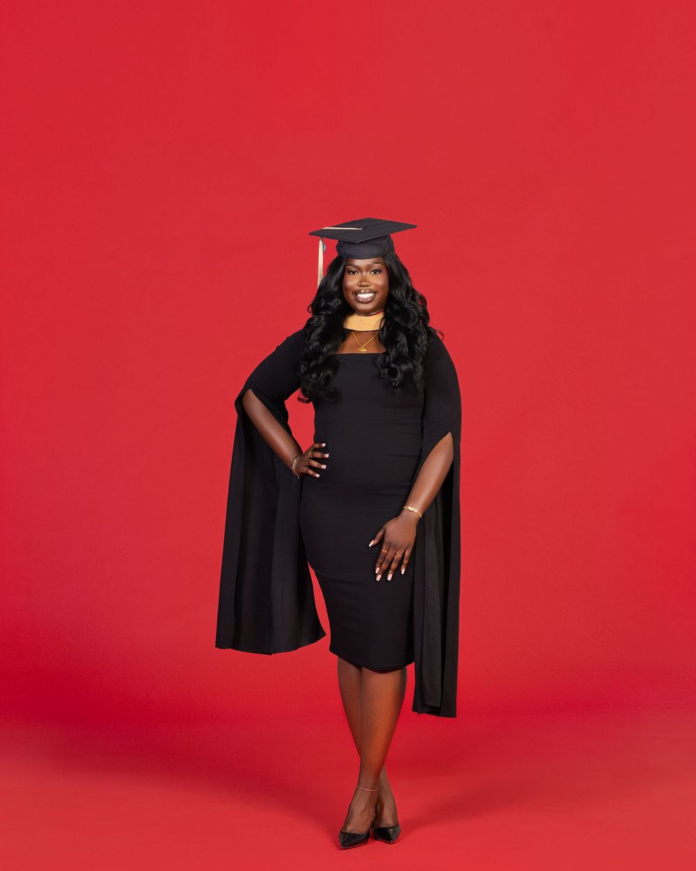 Graduate portrait session against vibrant red backdrop showing figure in black dress and graduation cap.