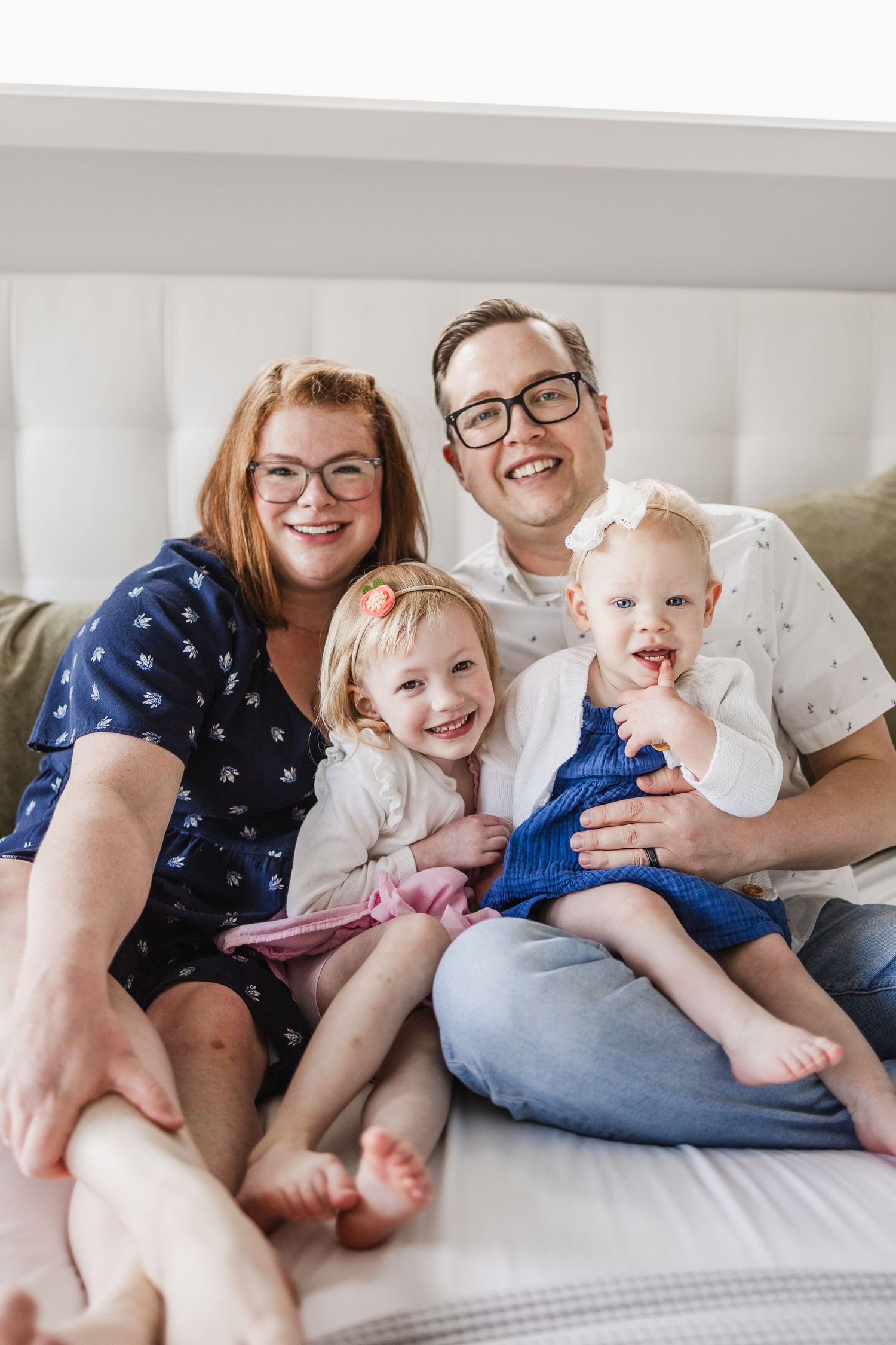 A family of four is smiling, posed for a photo snuggled up together on a bed