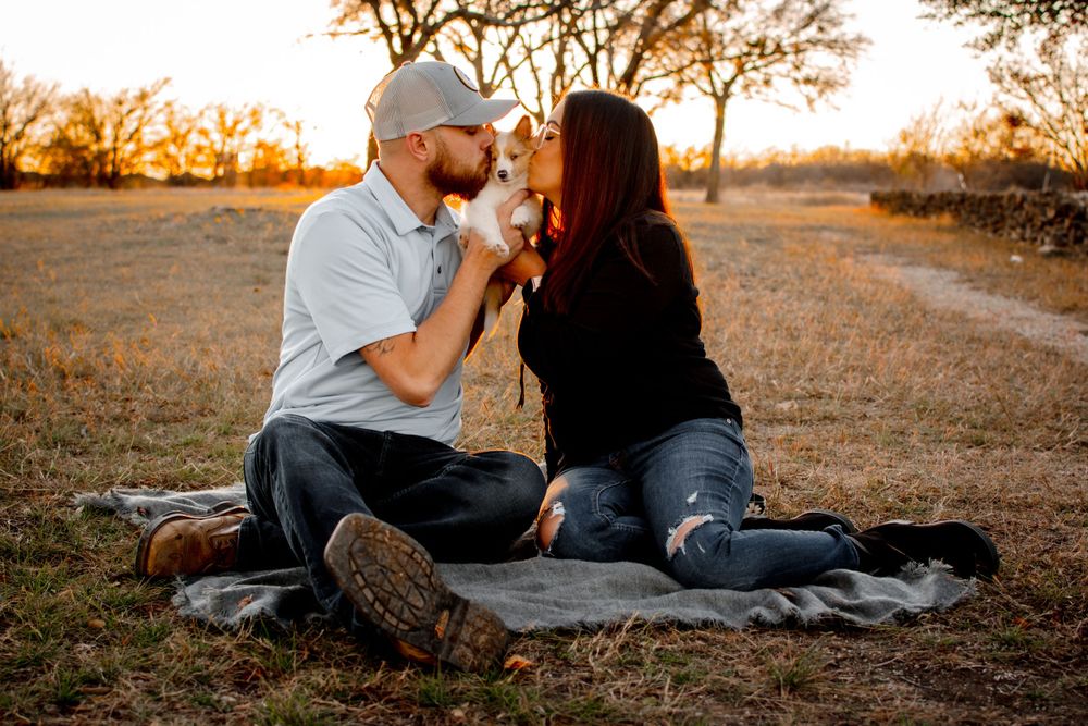 Couple sitting on blanket sharing a kiss with dog in the middle during sunset photo session in Dallas–Fort Worth