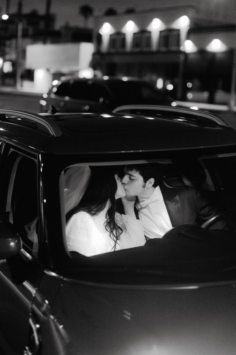 A romantic black and white photo of newlyweds in a vintage car at night.