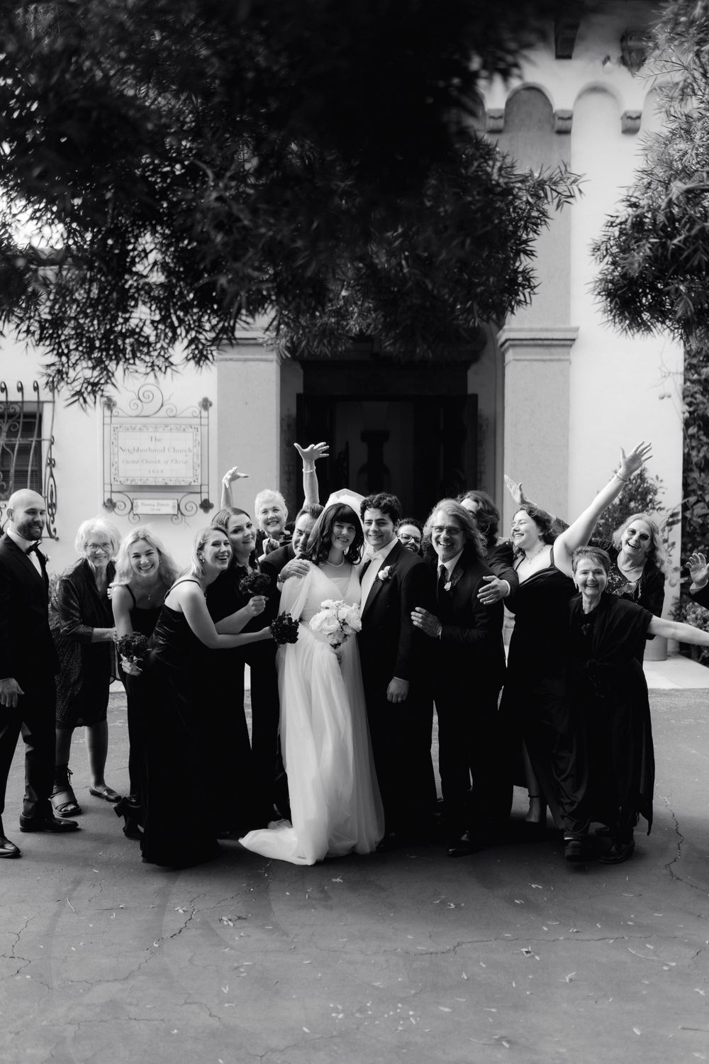 Black and white photo of wedding guests gathered outside a church building for a group portrait.