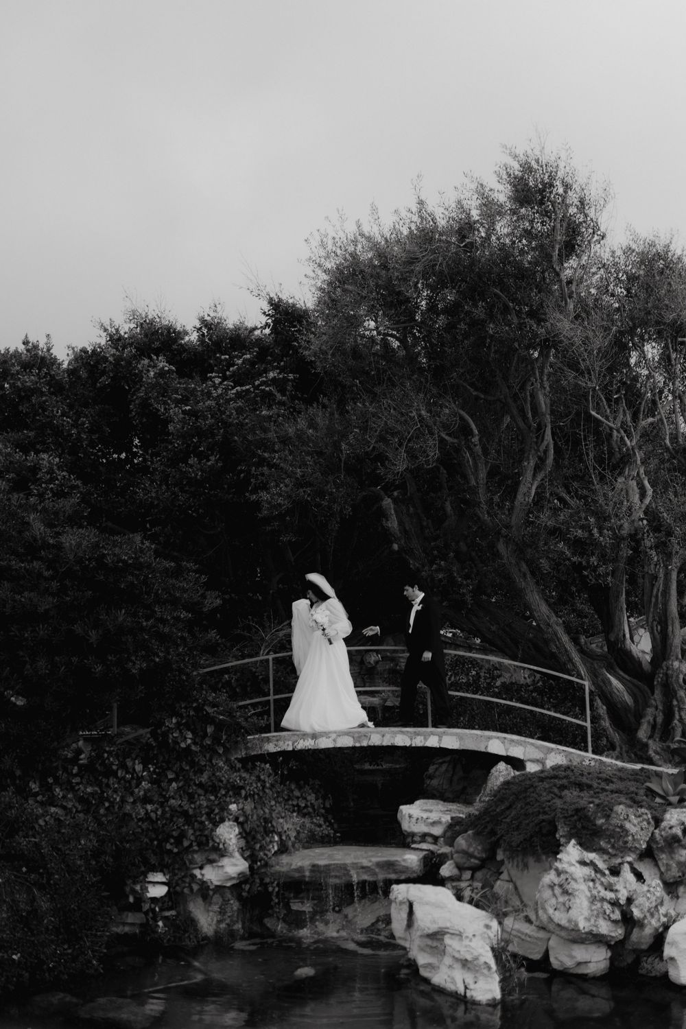 Black and white photo of newlyweds posing on a decorative garden bridge.