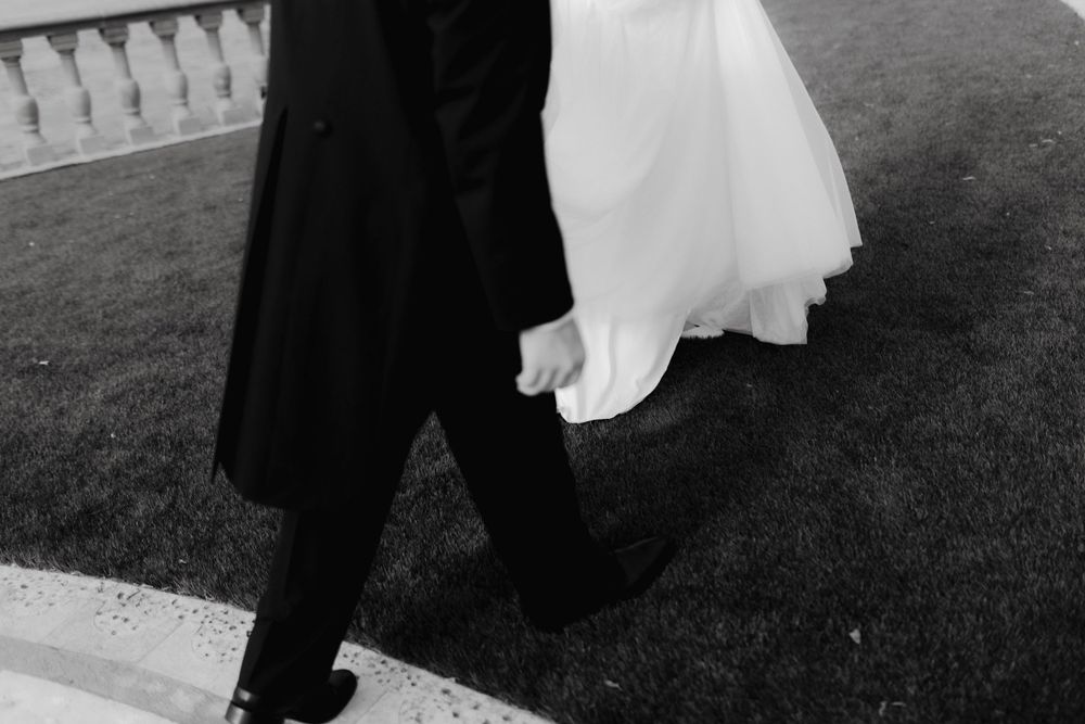 Wedding couple walks together on grassy path in formal attire.