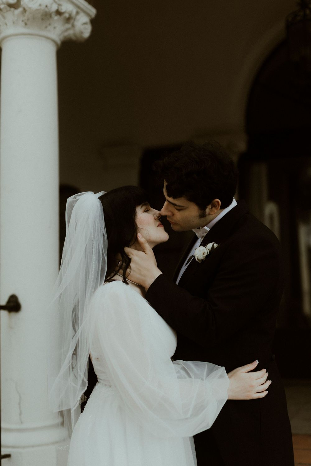 Newlyweds share tender moment among classical white columns.