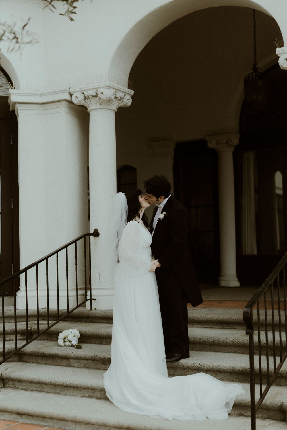 Wedding couple in dramatic pose by architectural columns and stairs.