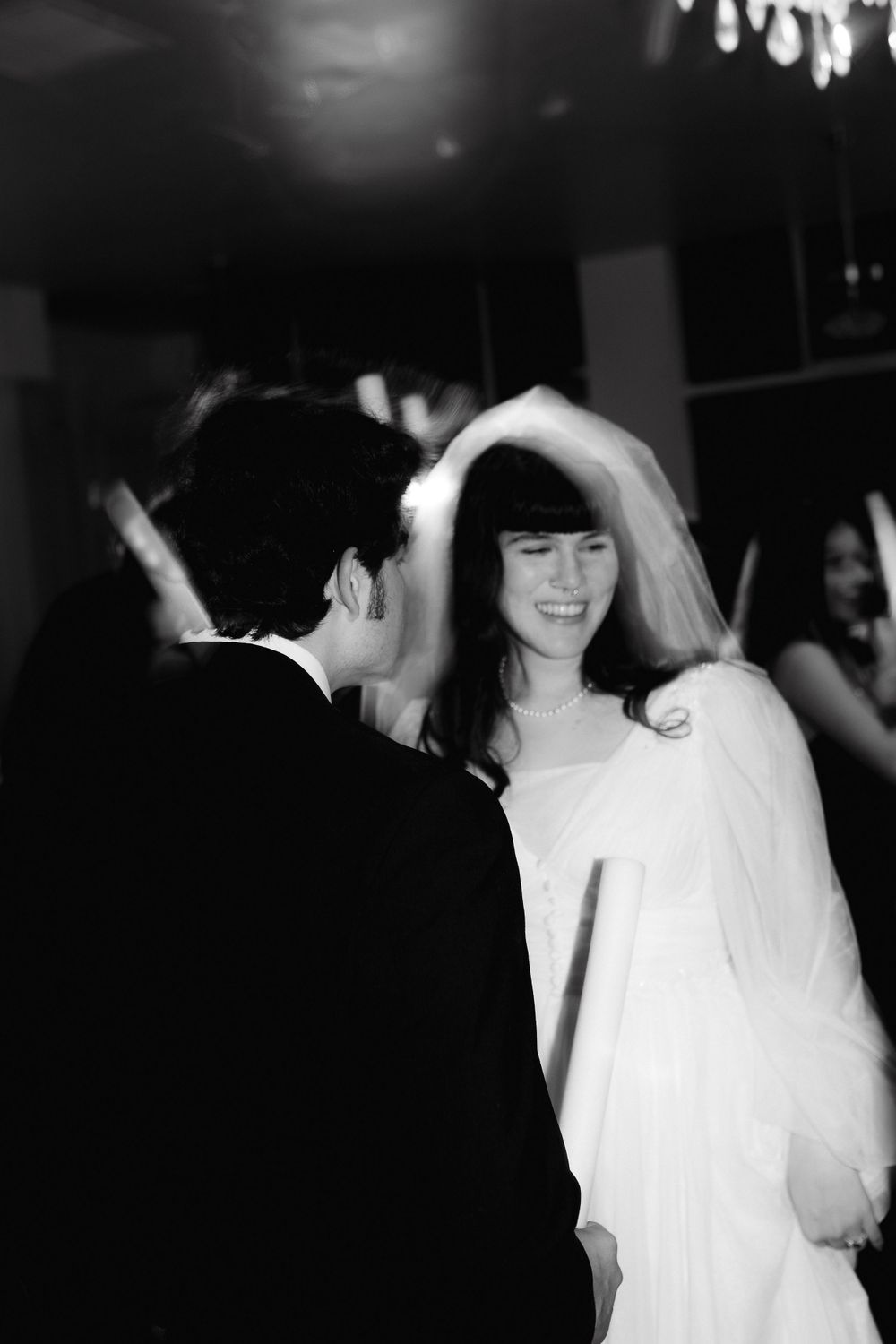 Bride in white dress and veil laughing during wedding reception.