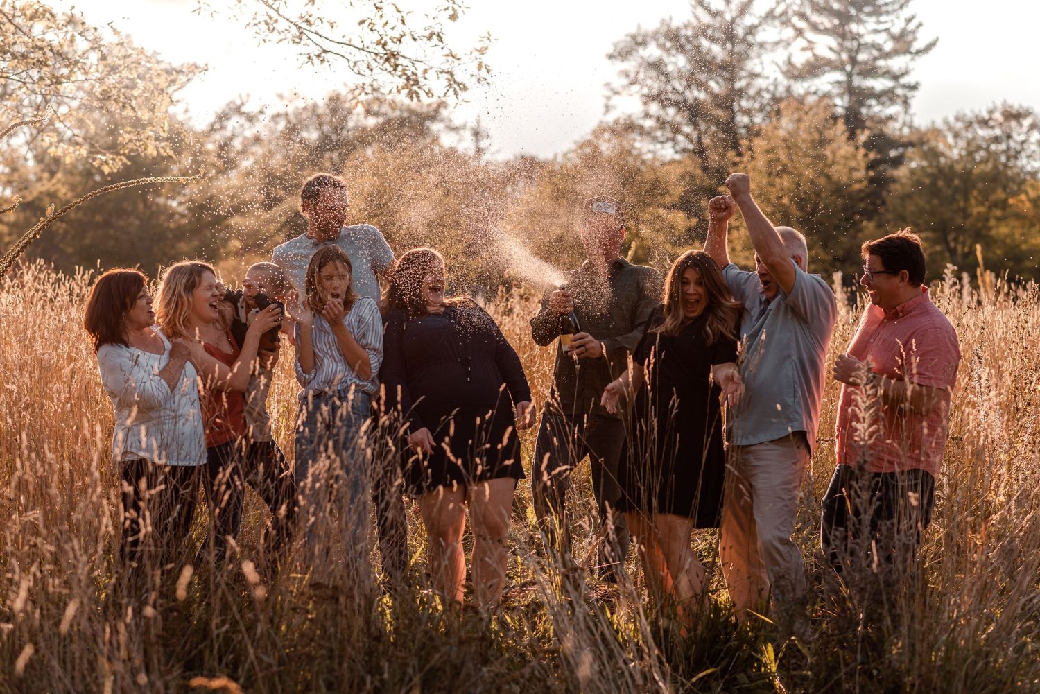 Group celebrating in tall grass field during golden hour sunset.