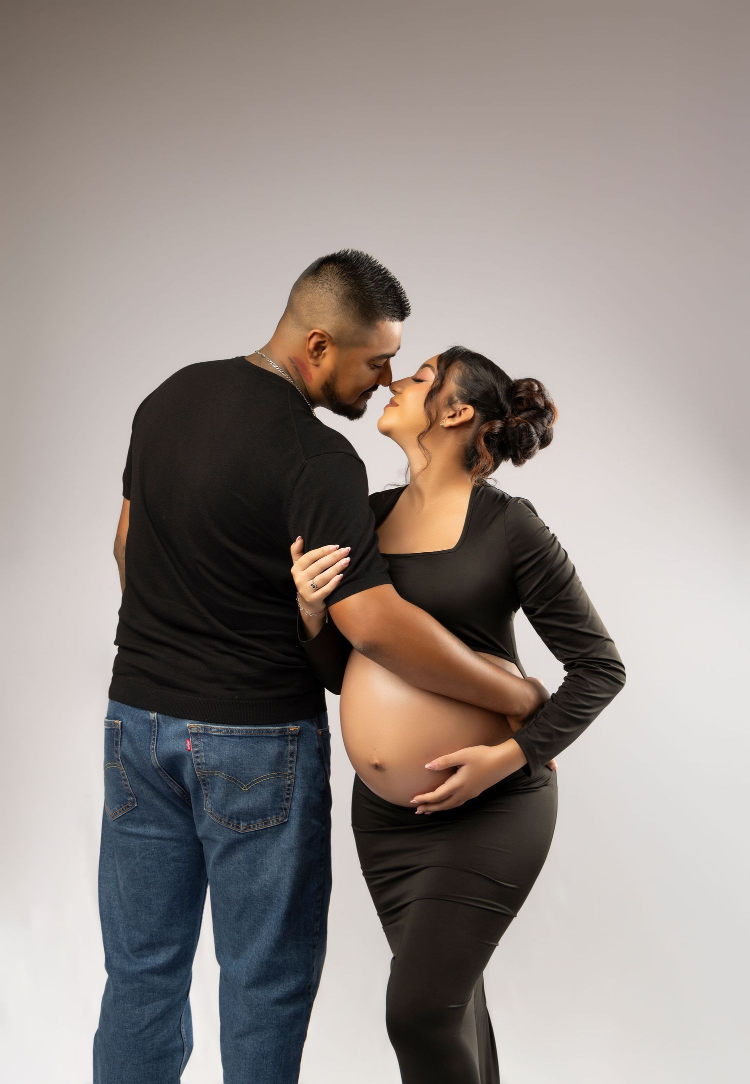 Maternity photo session with woman in flowing teal tulle gown against grey backdrop.