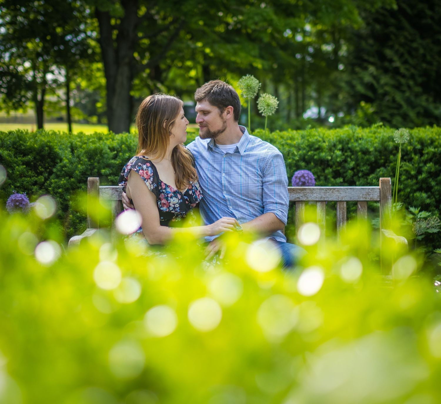 Romantic couple seen through bokeh lights in lush green garden setting.