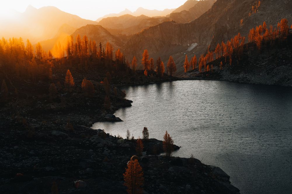 Sunset illuminates mountain landscape with alpine lake and forest silhouettes.
