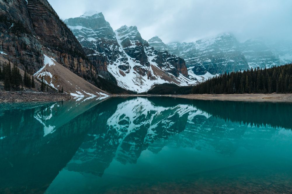 Mirror-like reflection of snow-covered mountains in turquoise waters of Moraine Lake, Banff.