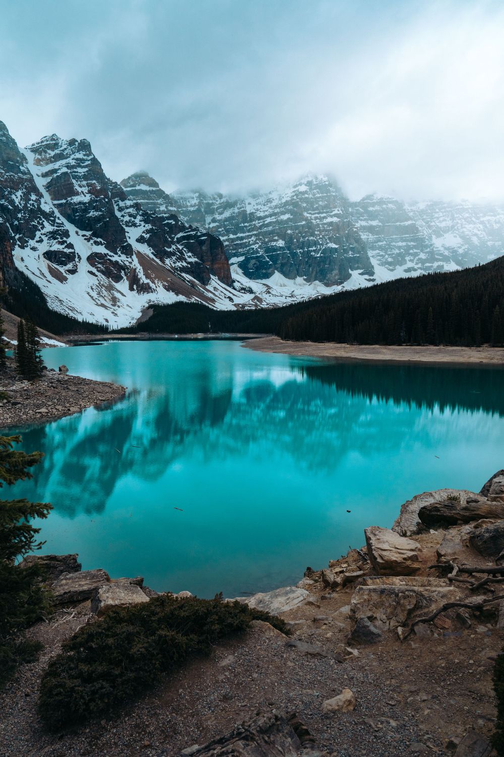 Snow-capped mountain peaks reflect in pristine turquoise waters of Moraine Lake in Canadian Rockies.