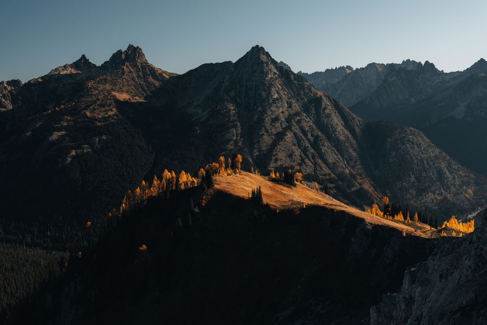 Golden sunlight illuminates mountain ridgeline with jagged peaks in dramatic shadow.
