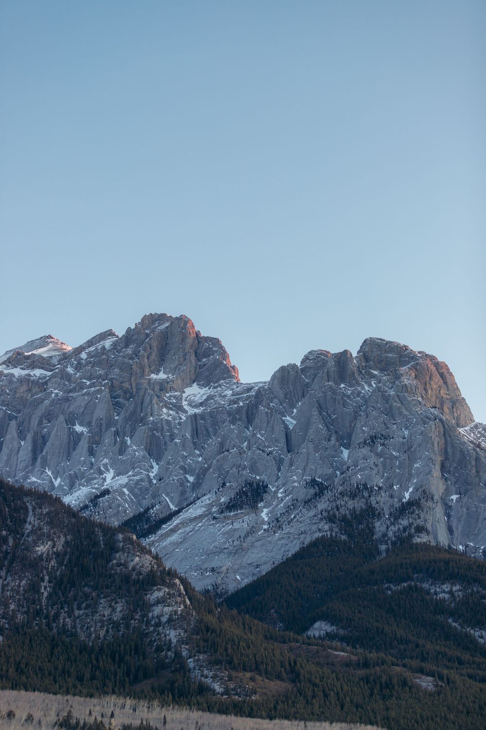 Snow-capped rugged mountain peaks rise against a clear blue sky in a dramatic alpine landscape.