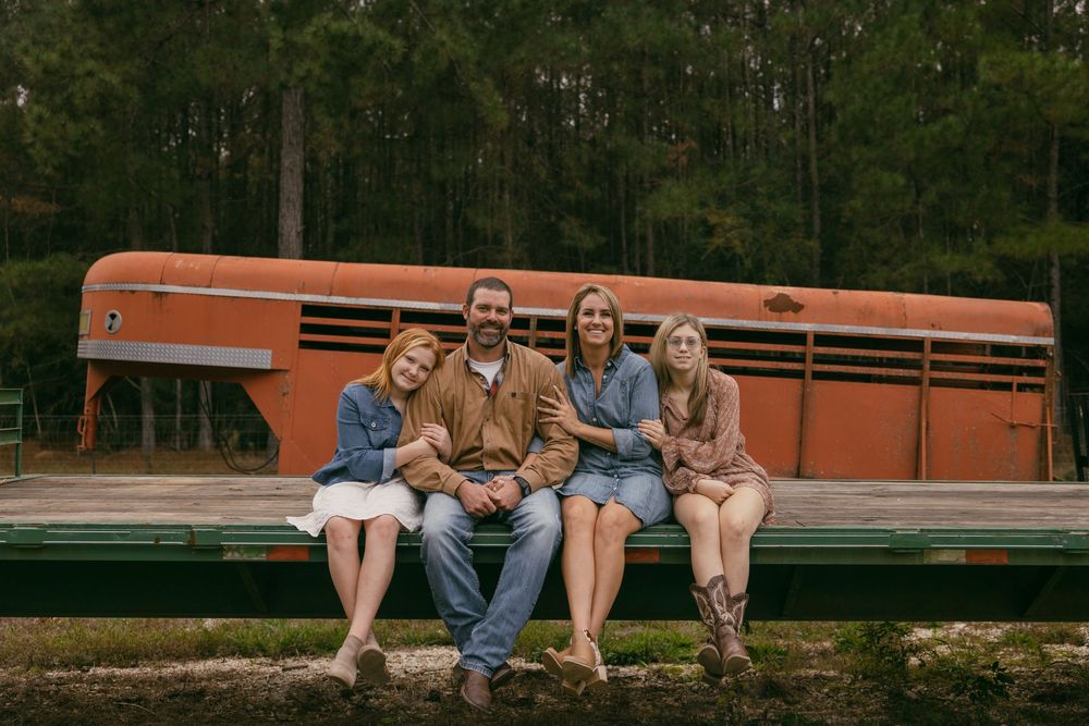 A group sits together on a bench against an orange bus in a wooded outdoor setting.