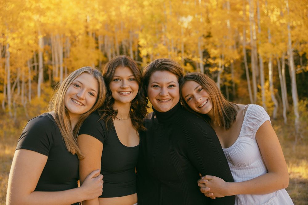 Four friends pose together outdoors with vibrant golden autumn aspen trees in the background.