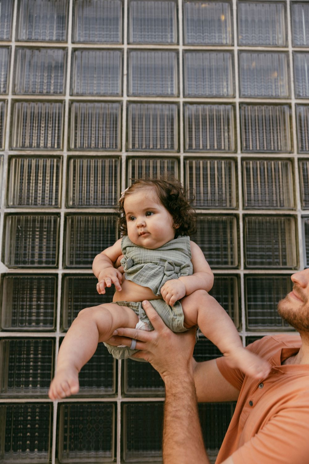 A series of photos showing someone holding a baby with a curly hairdo against a glass wall background.
