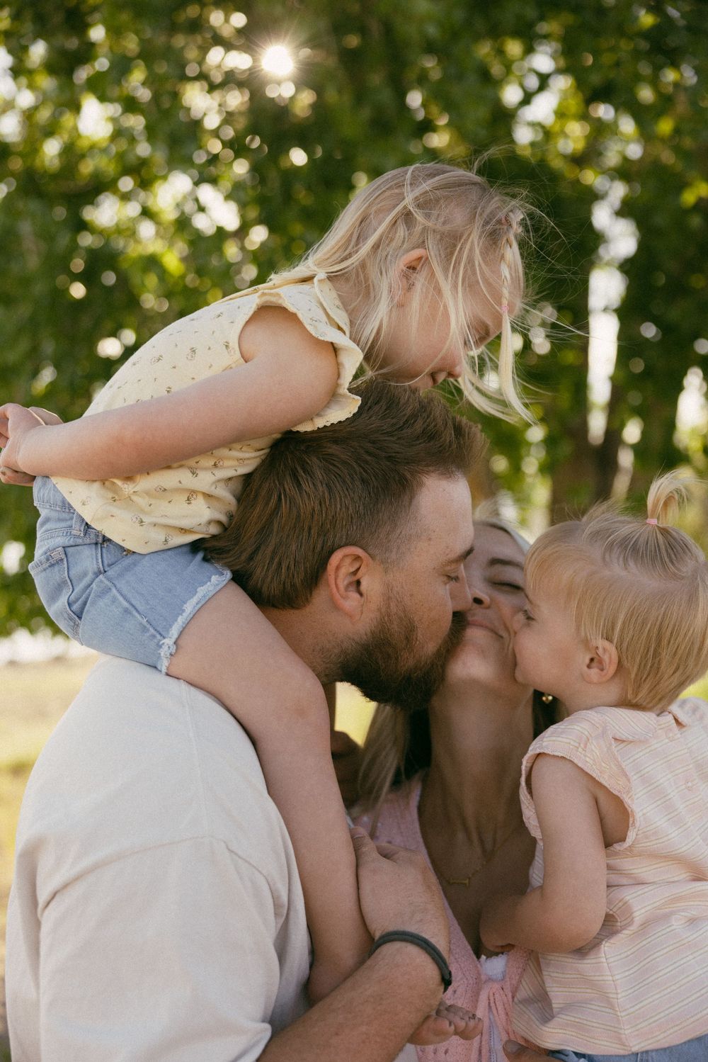 Intimate outdoor family portrait with sunlit bokeh through trees in the background during golden hour.