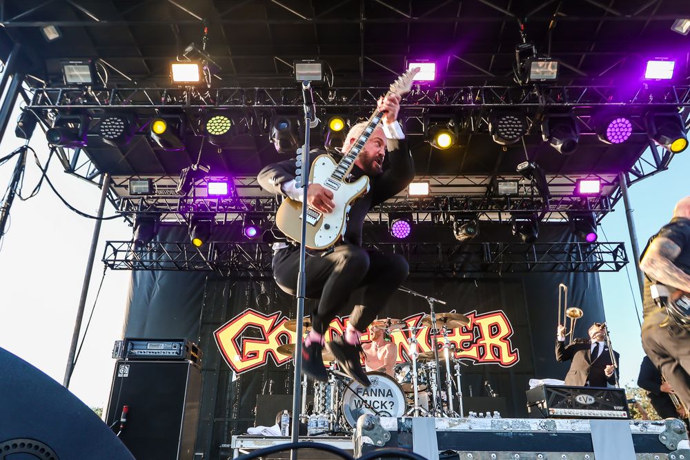 Live music photography of John Feldmann of Goldfinger jumping in the air with his guitar while performing on stage.