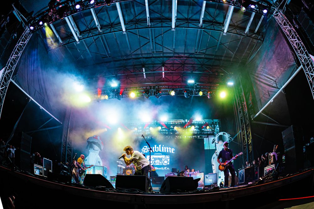 Band performing on a vibrant festival stage with colorful lights and fog effects at an outdoor music event.
