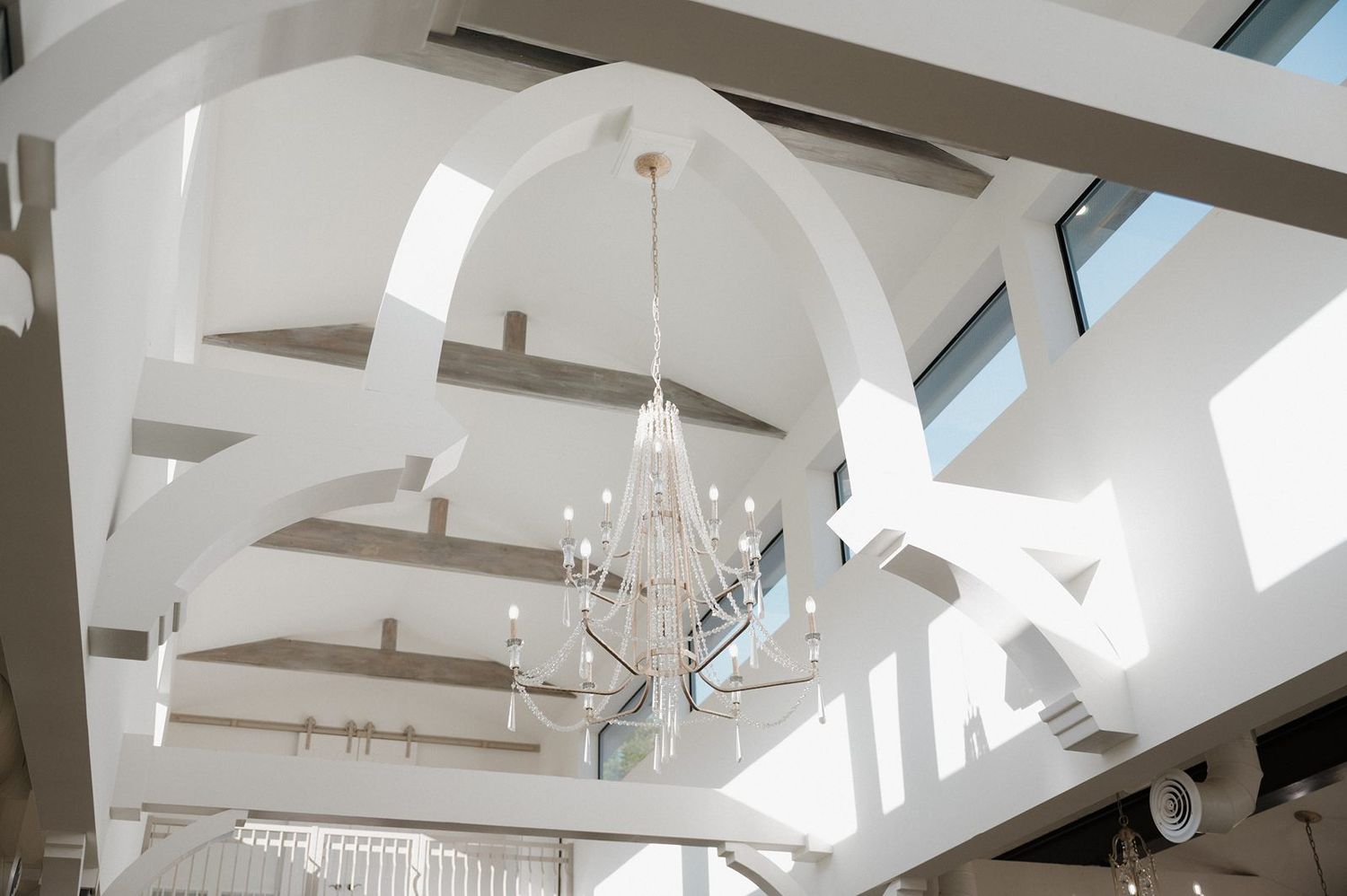 White vaulted ceiling with exposed wooden beams and a crystal chandelier in an elegant bright interior space.
