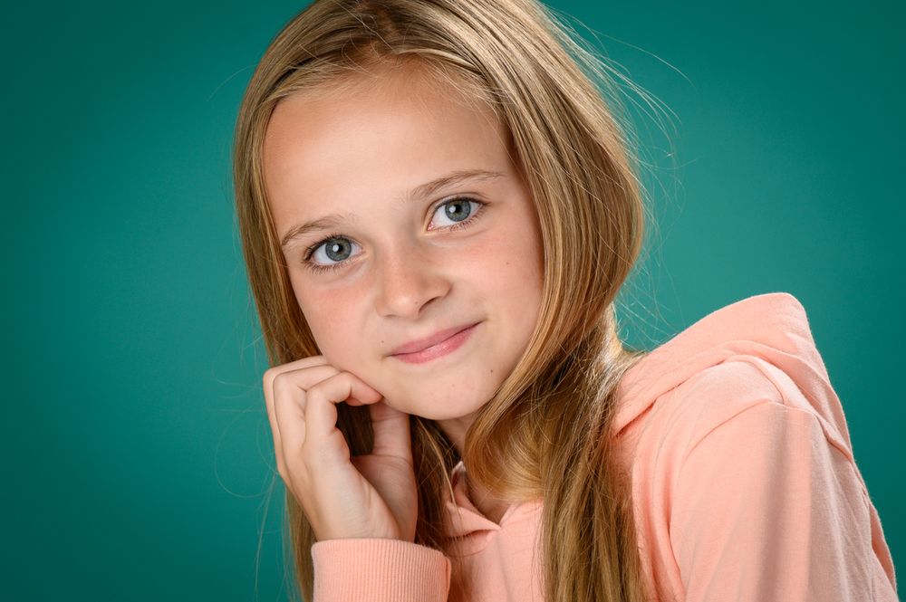 Young student in peach colored top poses against turquoise backdrop.