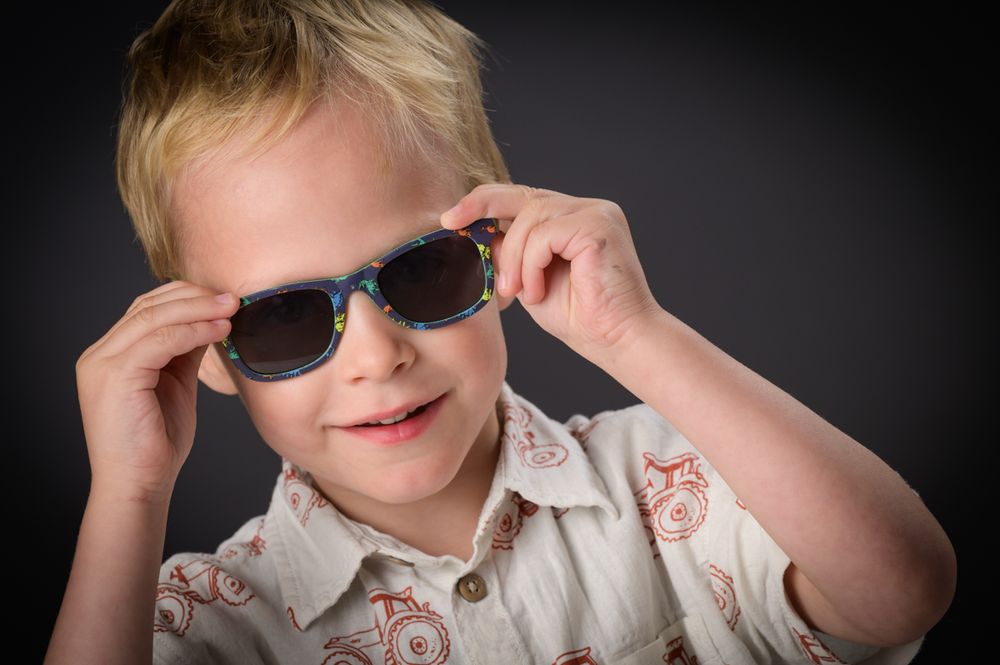 Playful sequence showing a child wearing sunglasses and a light colored shirt against a dark background.