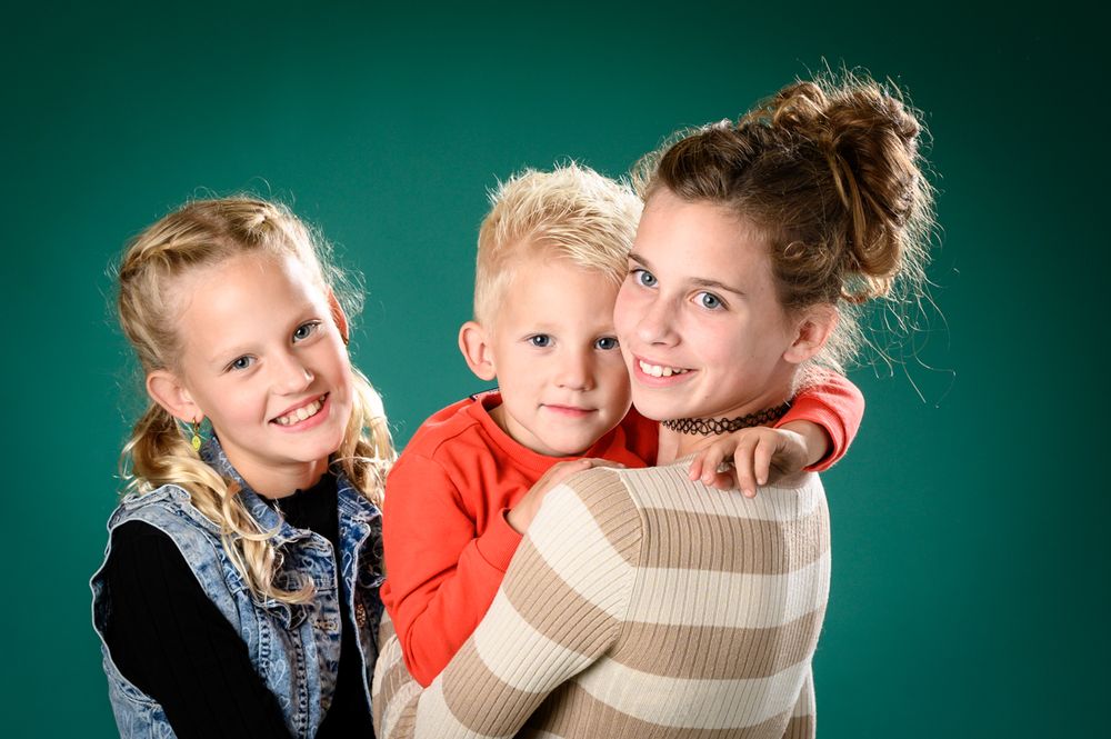 Group portrait with children in casual winter wear against teal background.