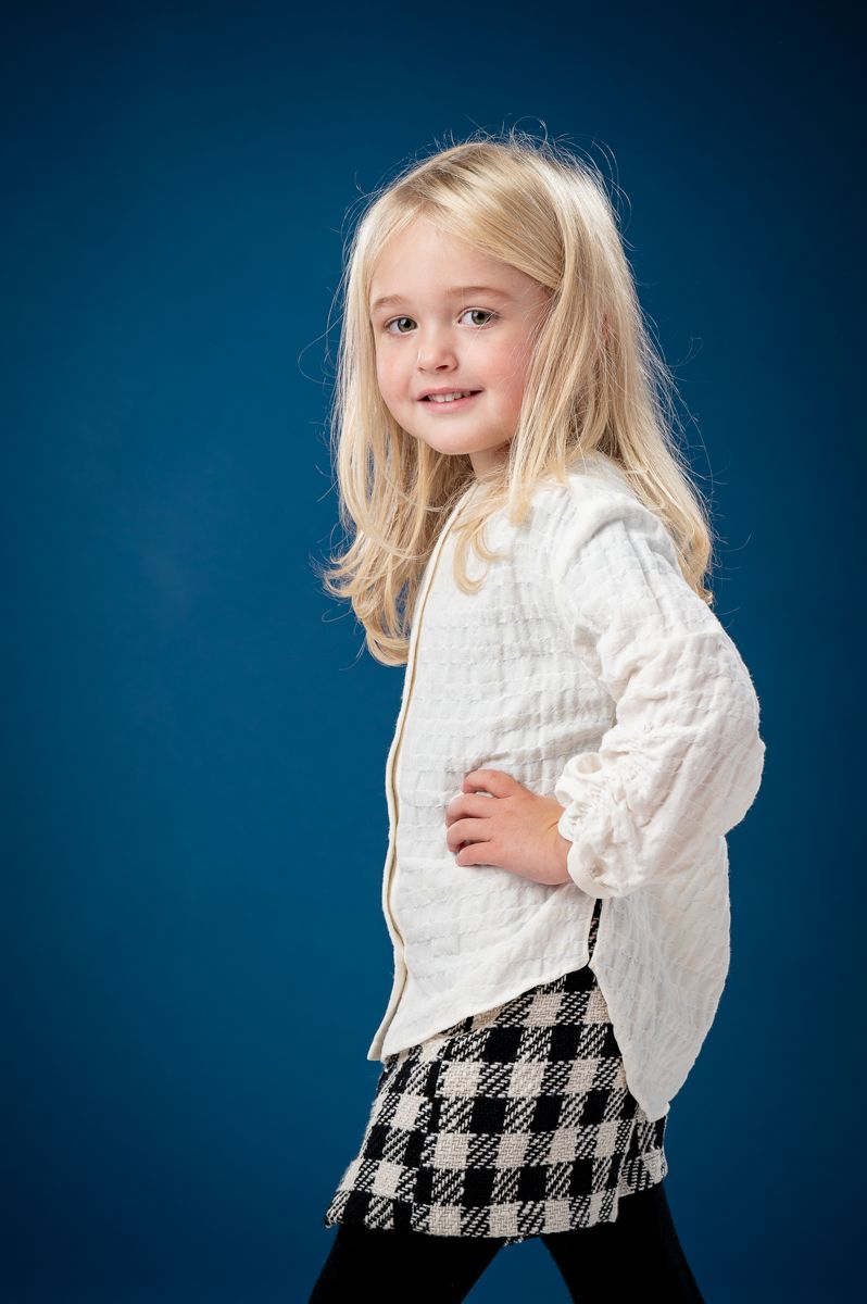 Child in white top and houndstooth pattern poses against blue background.
