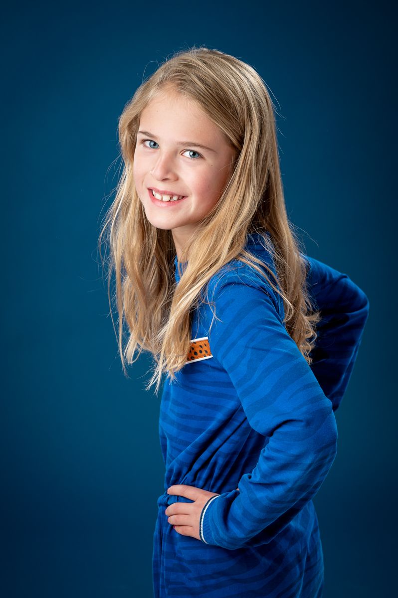 Child in bright blue hoodie poses playfully against dark blue background.
