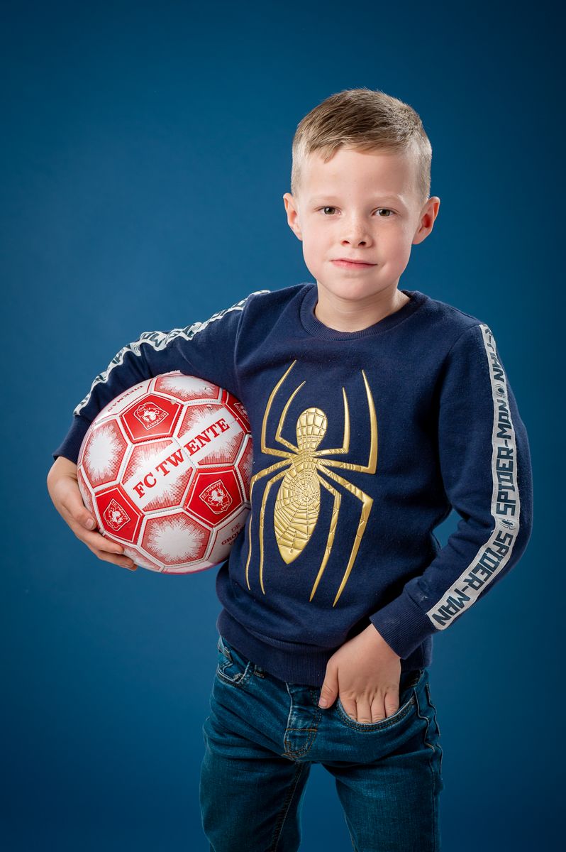 Young sports fan wearing navy Spider-Man shirt holds red soccer ball.