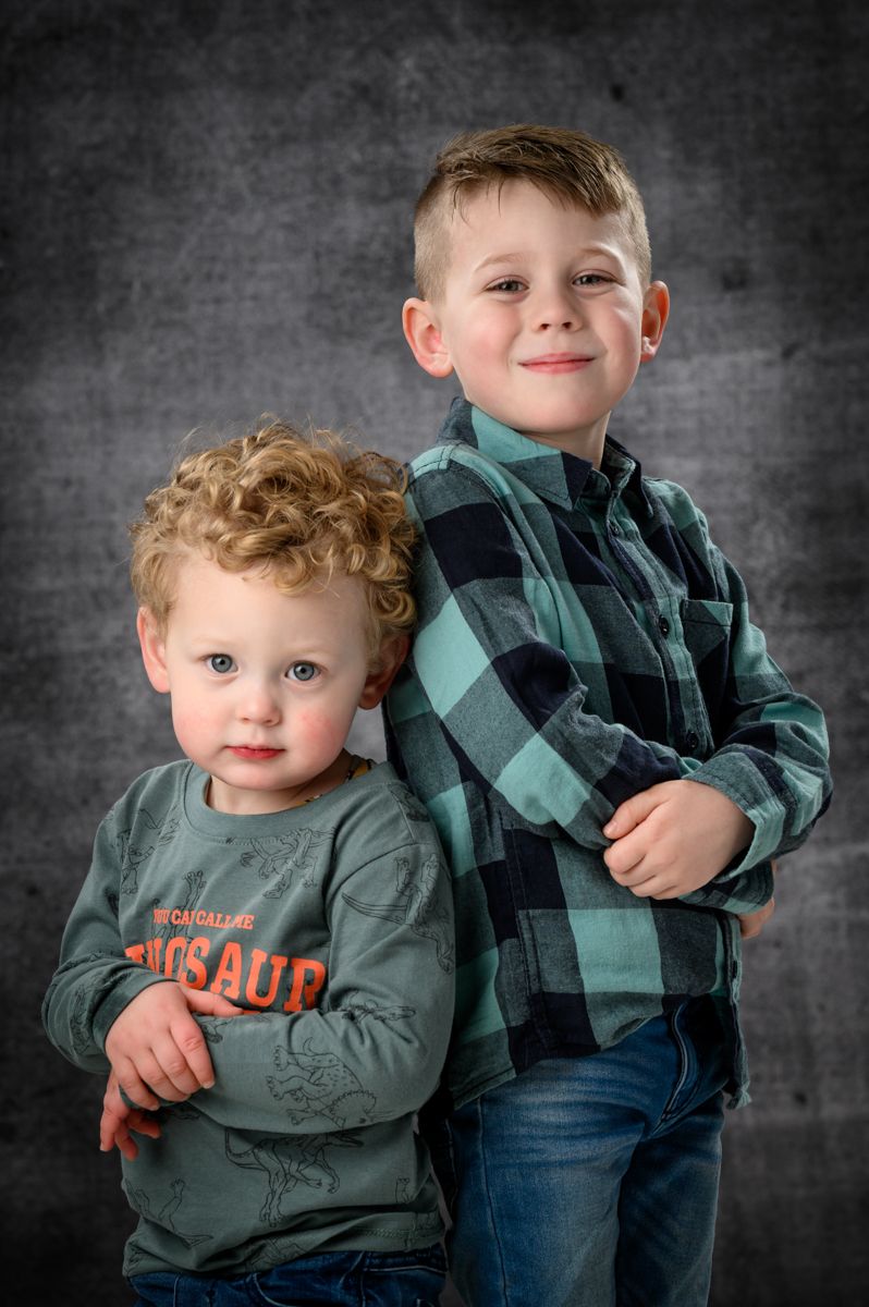 Two children in matching green plaid shirts pose together against grey background.