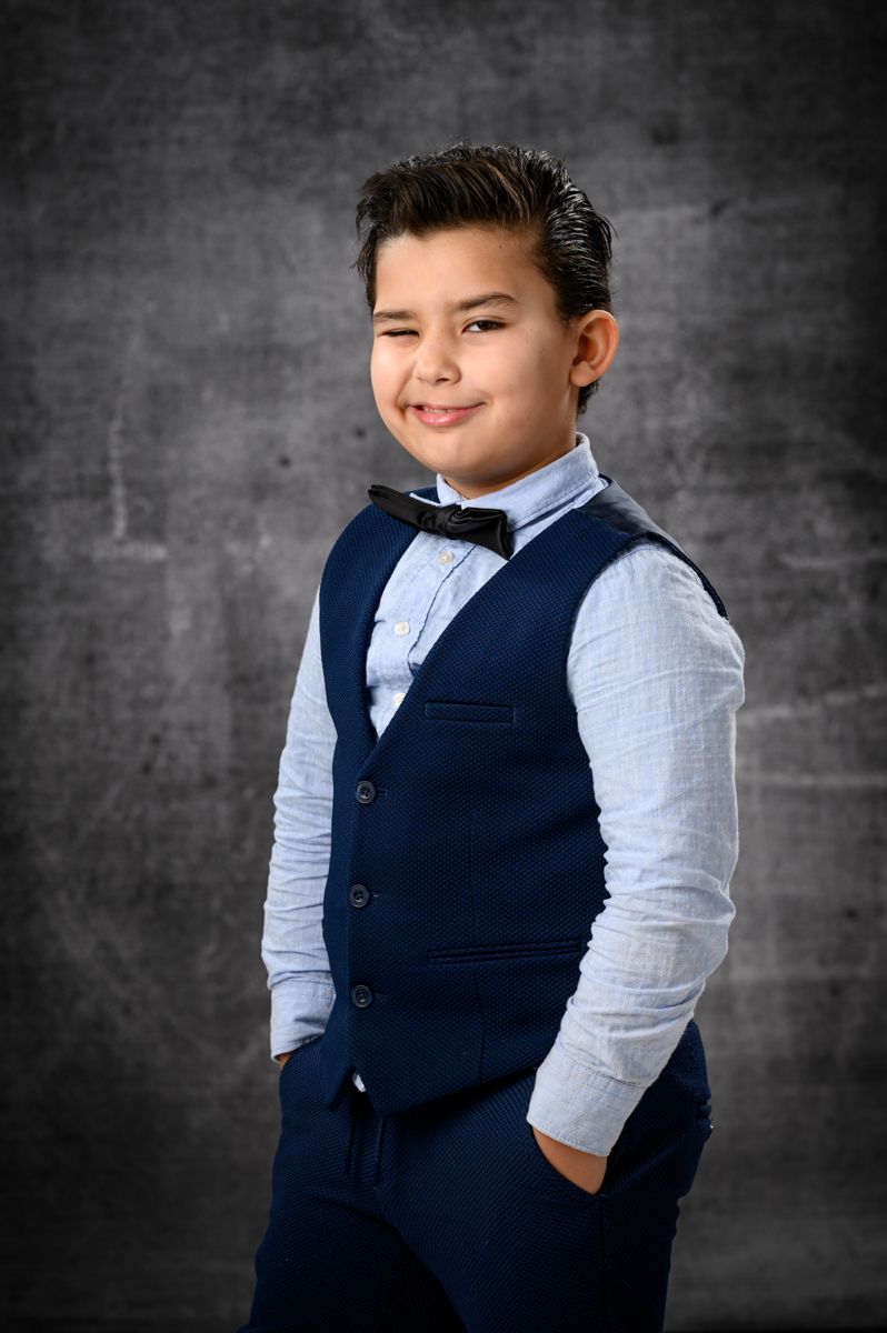 Young person in formal navy vest and white shirt poses confidently.