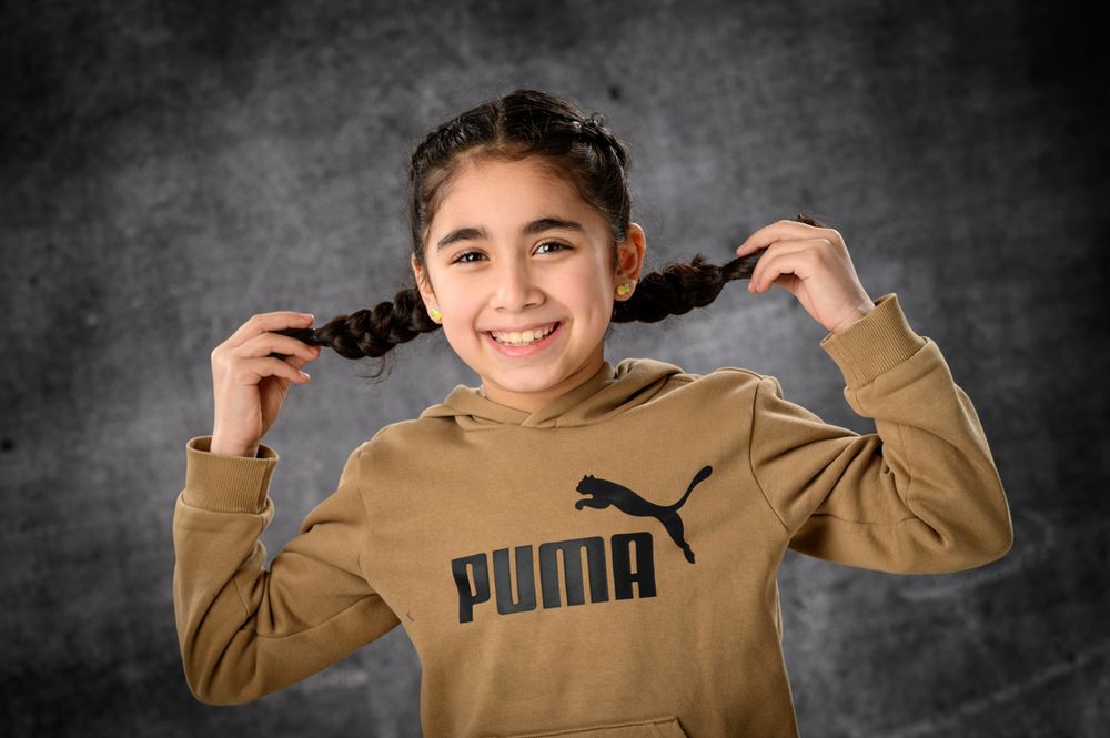 Youth in tan Puma sweatshirt poses playfully against dark background.