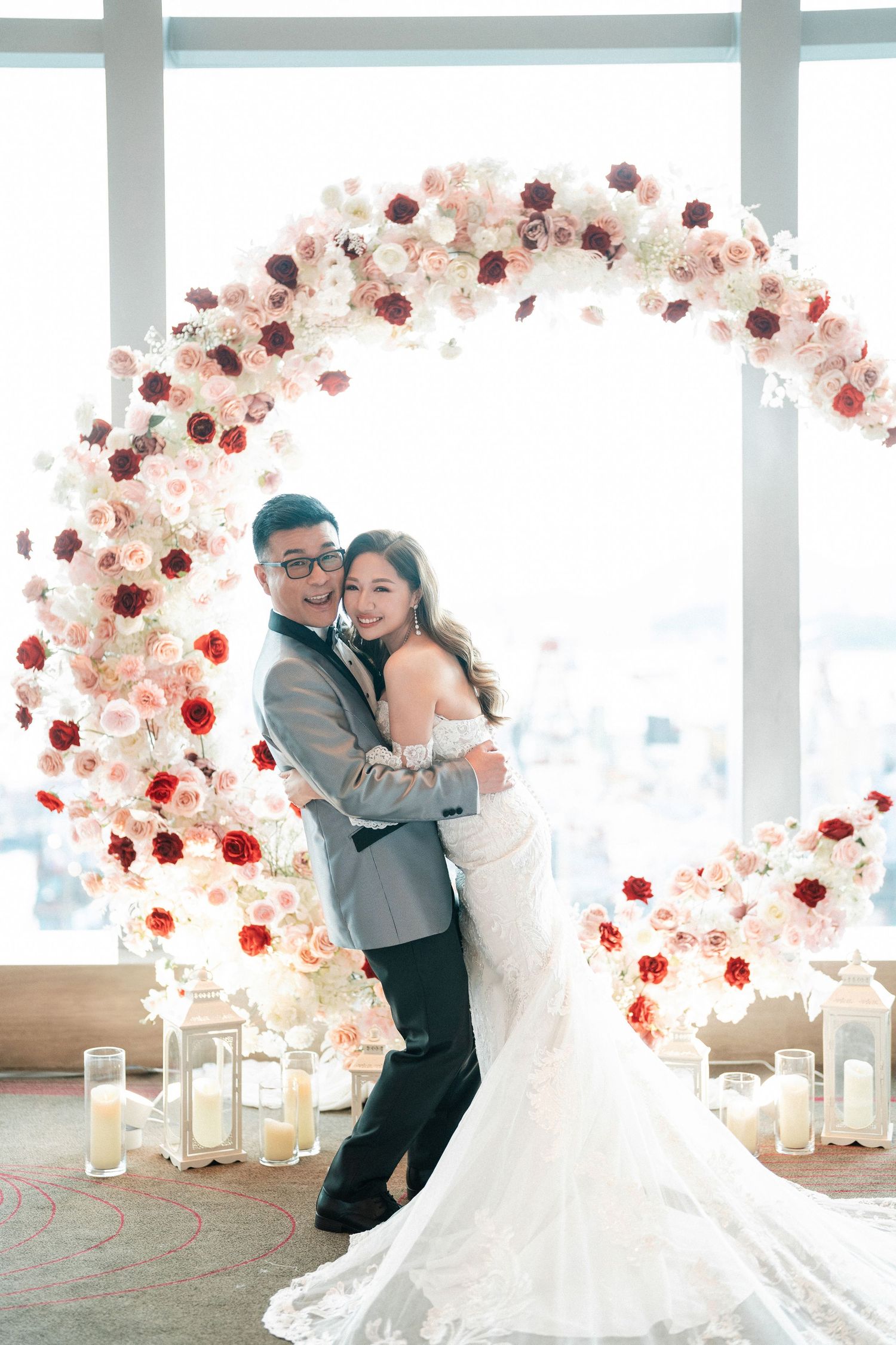 A couple poses under a circular floral arch with pink and white roses at their wedding.
