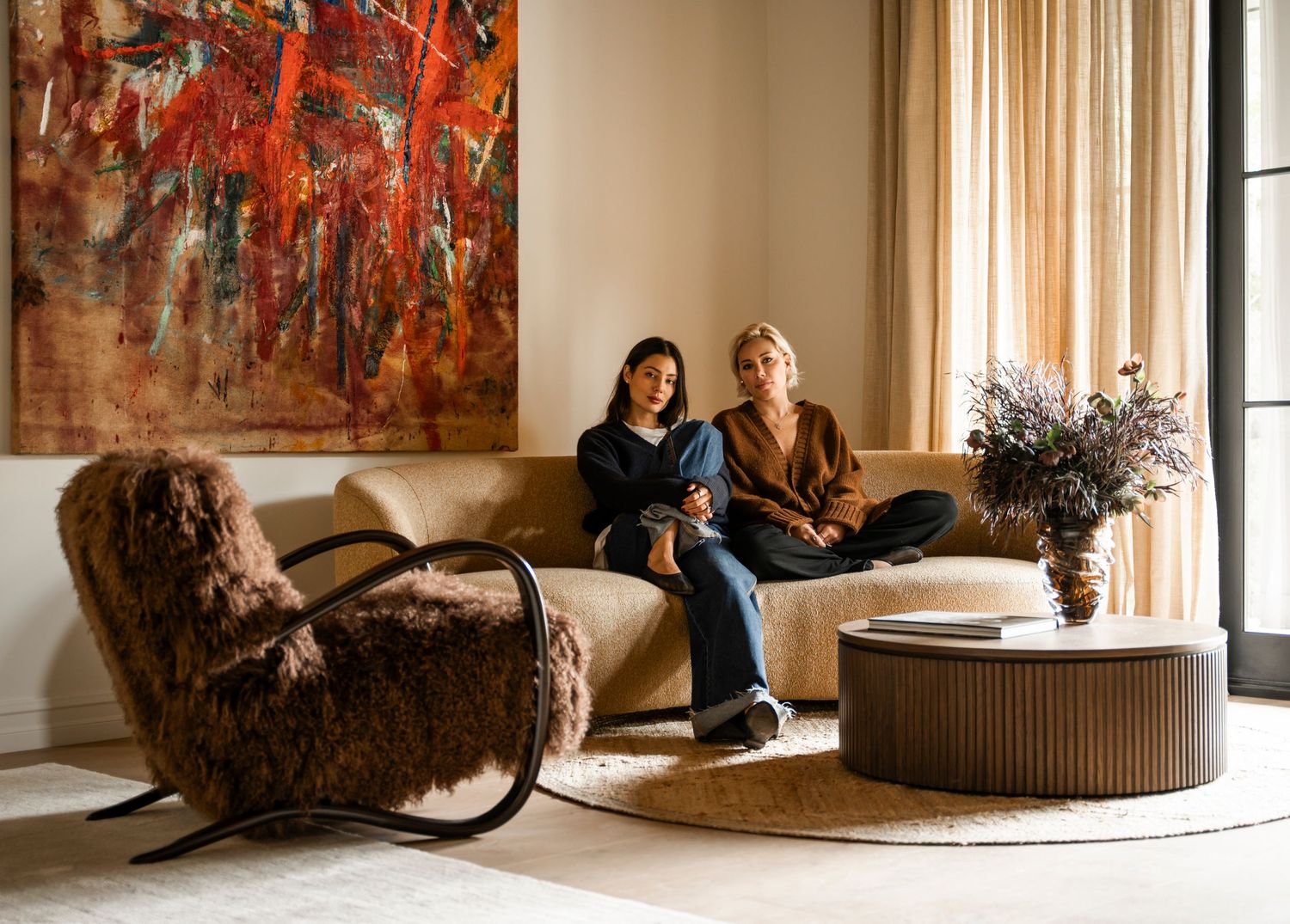 A stylishly decorated lounge space with orange abstract art and modern furniture in a sunlit room.