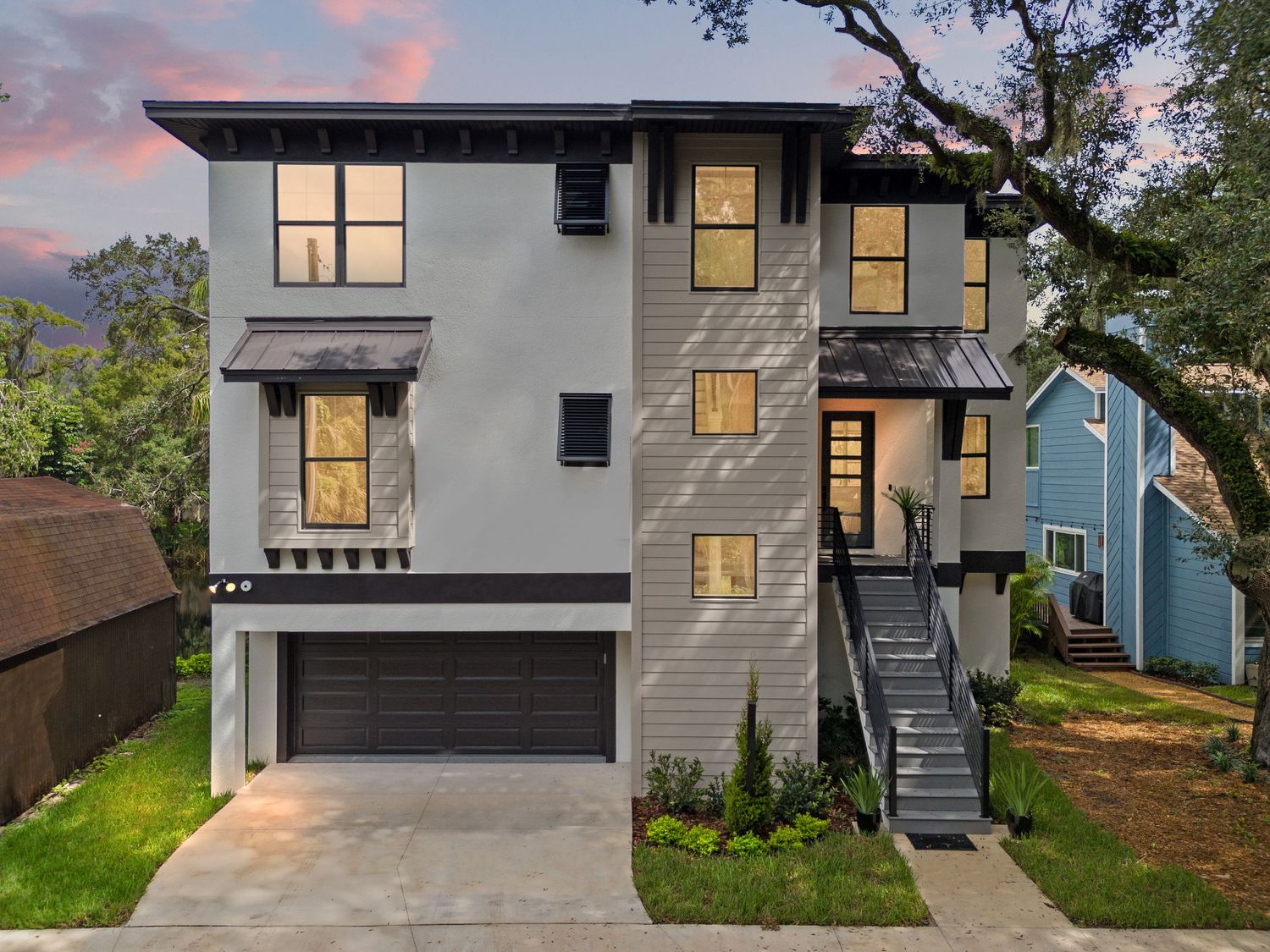 Modern two-story home exterior with white and dark trim features illuminated windows at dusk.