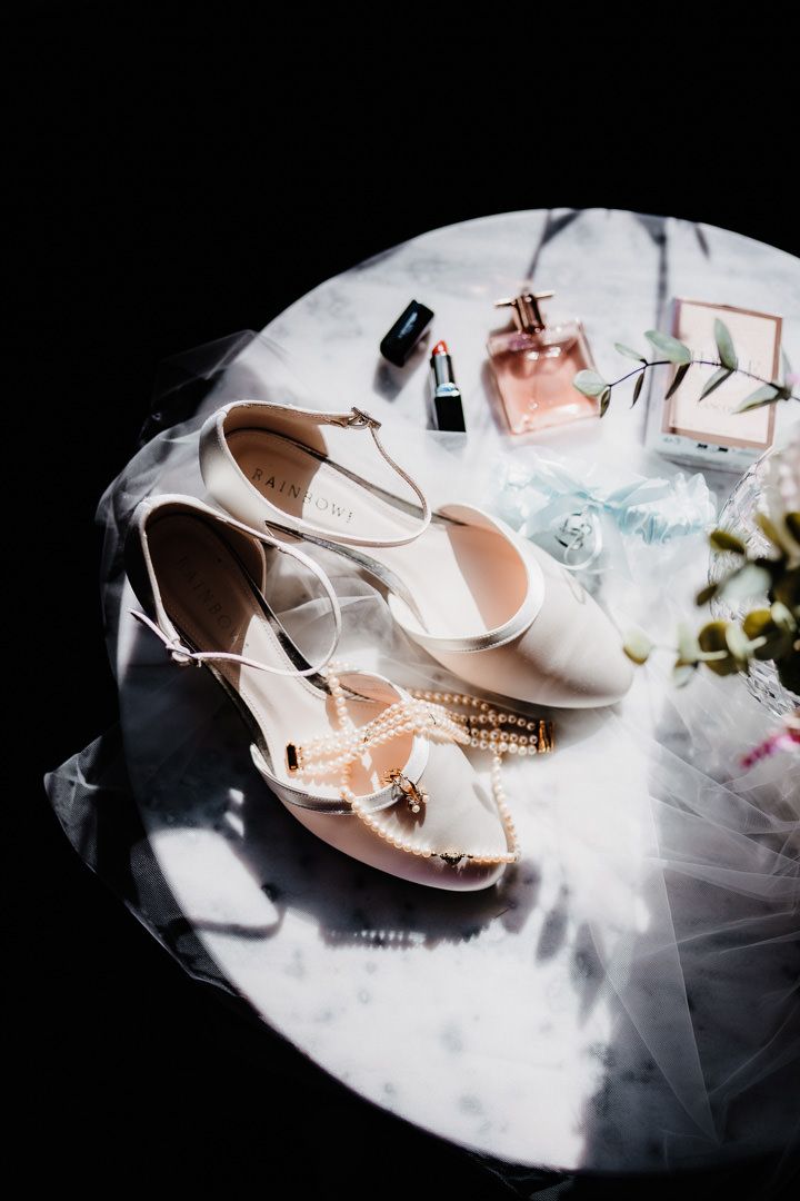 Wedding accessories including white shoes, perfume and makeup on tulle fabric.
