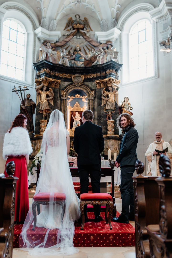 Wedding ceremony in baroque church with elaborate golden altar and white architectural details.