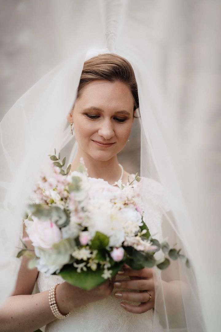 An elegant bridal portrait with a flowing veil and delicate floral bouquet.