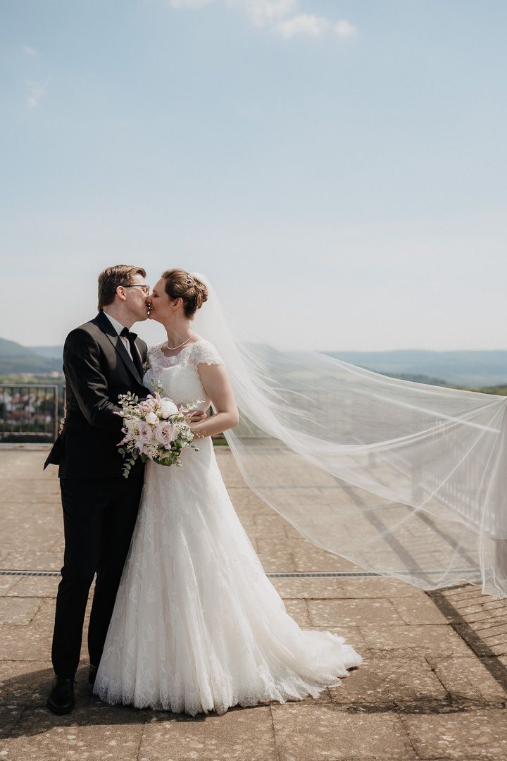 Romantic wedding portrait with veil flowing in the wind against a scenic mountain landscape.