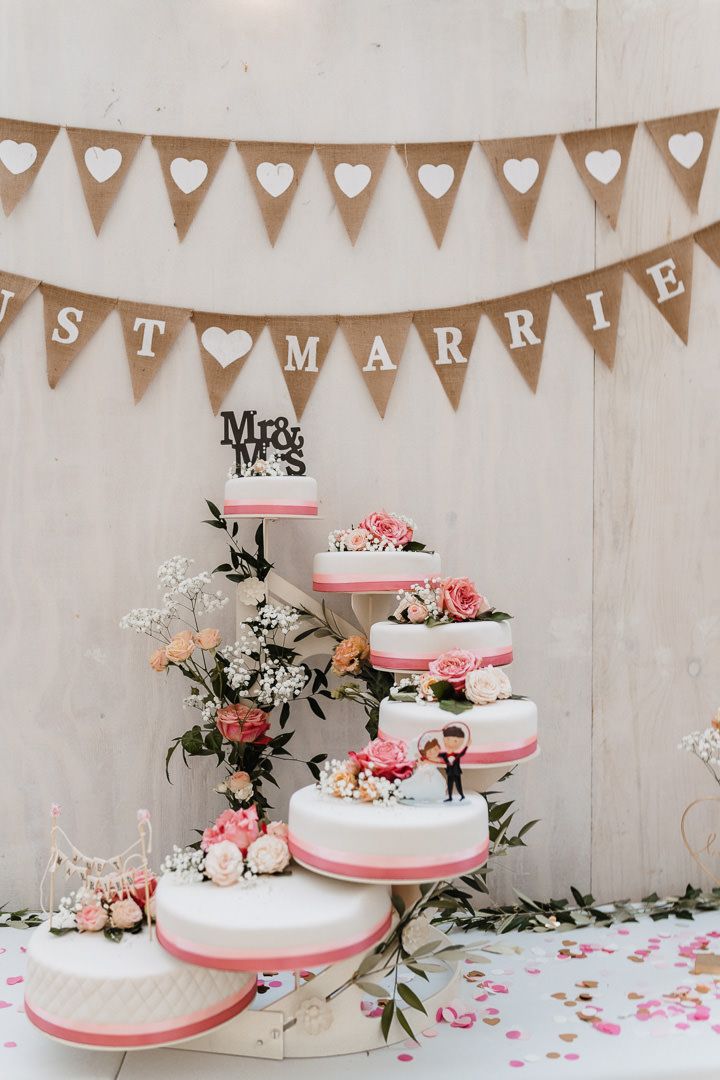 Elegant multi-tiered white wedding cake with pink trim under Just Married burlap bunting.