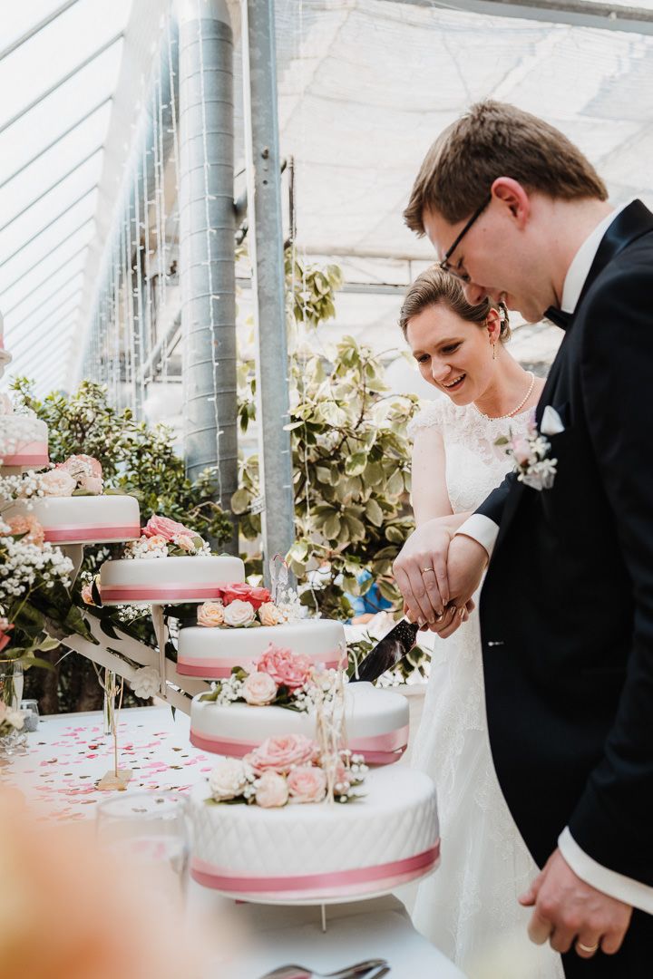 Couple cutting into their elegant tiered wedding cake with pink accents and floral decorations.