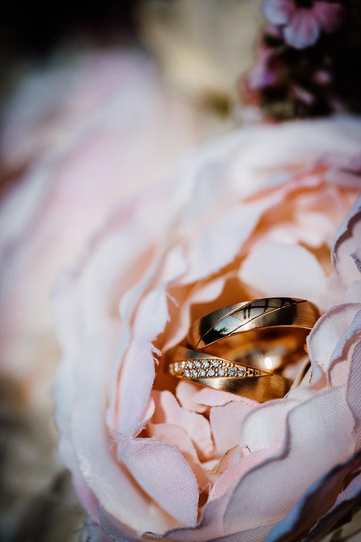 Wedding rings with diamond details captured inside blush rose petals.