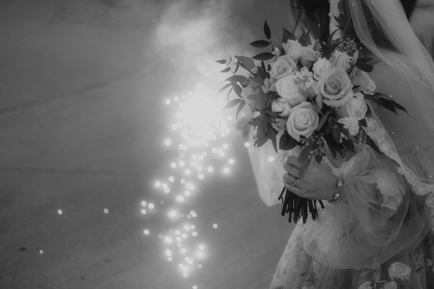 Black and white image of bridal bouquet with sparkly bokeh lights.