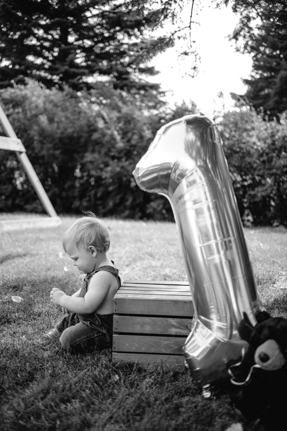 Black and white photos of a small child playing with a large metallic container outdoors.